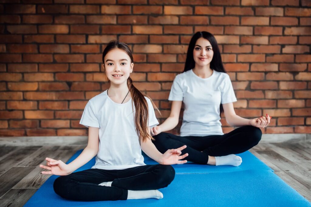 two young sisters practicing yoga position indoor gym studio healthy wellness lifestyle concept